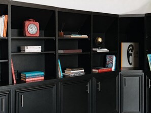 A black bookshelf with various books, a red clock, and a globe.