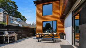 Ein modernes Gebäude mit Holzfassade, einer Terrasse mit Grill und Picknicktisch sowie einer Garagentür.