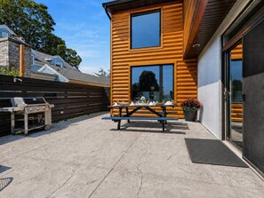 Ein modernes Gebäude mit Holzfassade, einer Terrasse mit Grill und Picknicktisch sowie einer Garagentür.