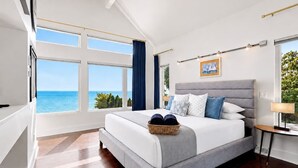 Ein modernes Schlafzimmer mit einem großen Bett, Meerblick und einem Fenster mit Vorhängen.