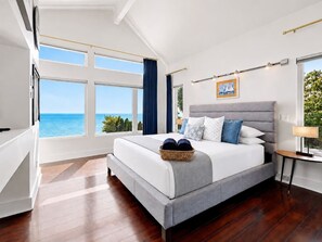 Ein modernes Schlafzimmer mit einem großen Bett, Meerblick und einem Fenster mit Vorhängen.