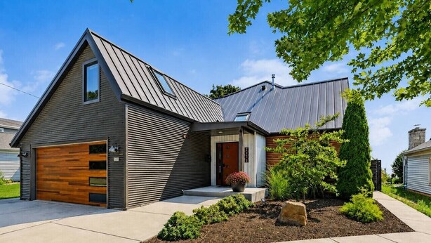 Ein modernes, zweistöckiges Haus mit Garage, Veranda und einem angelegten Garten.