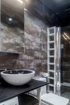 A modern bathroom with a large mirror, a white sink with a black countertop, and a glass shower enclosure. - Intimate rooftop terrace with a hot tub and 360° views of Barcelona (Barcelona)