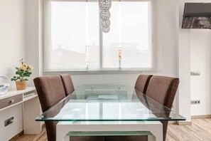 A modern kitchen with a glass-top dining table, two brown chairs, a small plant, and a window with a decorative light fixture. - Intimate rooftop terrace with a hot tub and 360° views of Barcelona (Barcelona)