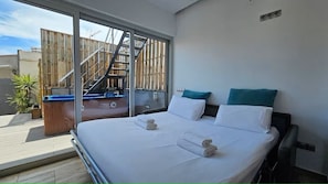 A hotel room with a large bed, two pillows, a wooden headboard, a sliding glass door leading to a balcony, and a small wooden table. - Intimate rooftop terrace with a hot tub and 360° views of Barcelona (Barcelona)