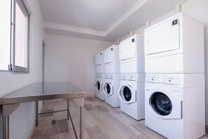 A laundry room with multiple washing machines and dryers, a metal table, and a window. - Luxury loft in the heart of Playa del Carmen Stunning Rooftop Pool and Jacuzzi (Playa del Carmen)