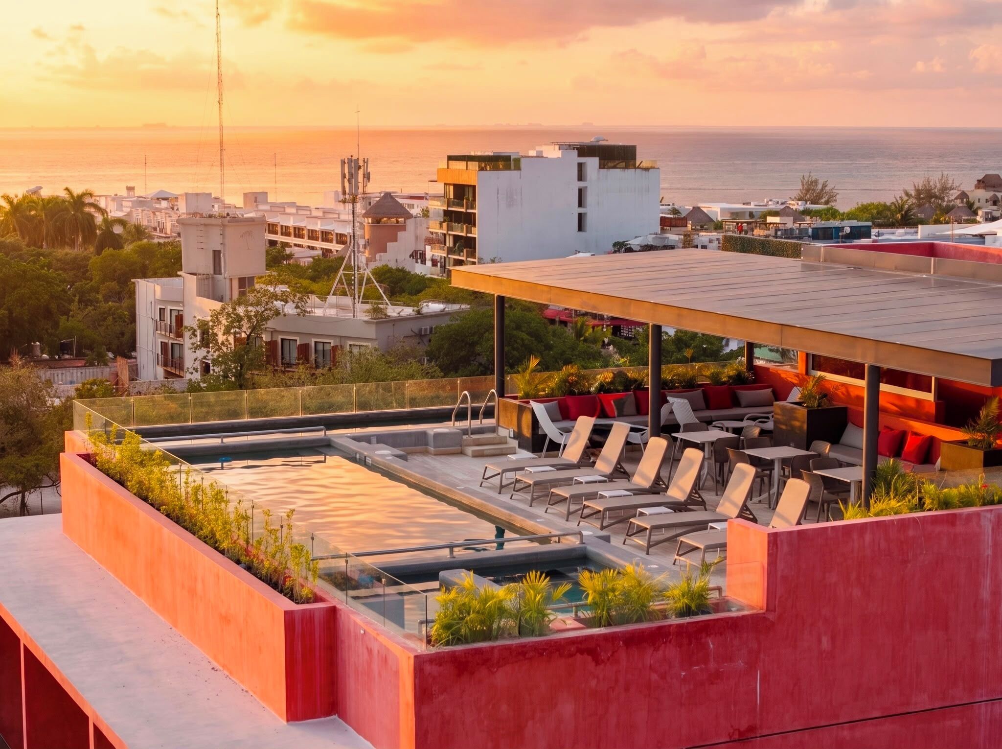A rooftop terrace with a pool, lounge chairs, and a view of the sea and cityscape.