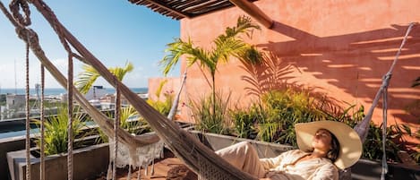 Un hamac sur une terrasse en bois, avec vue sur la ville et les palmiers.