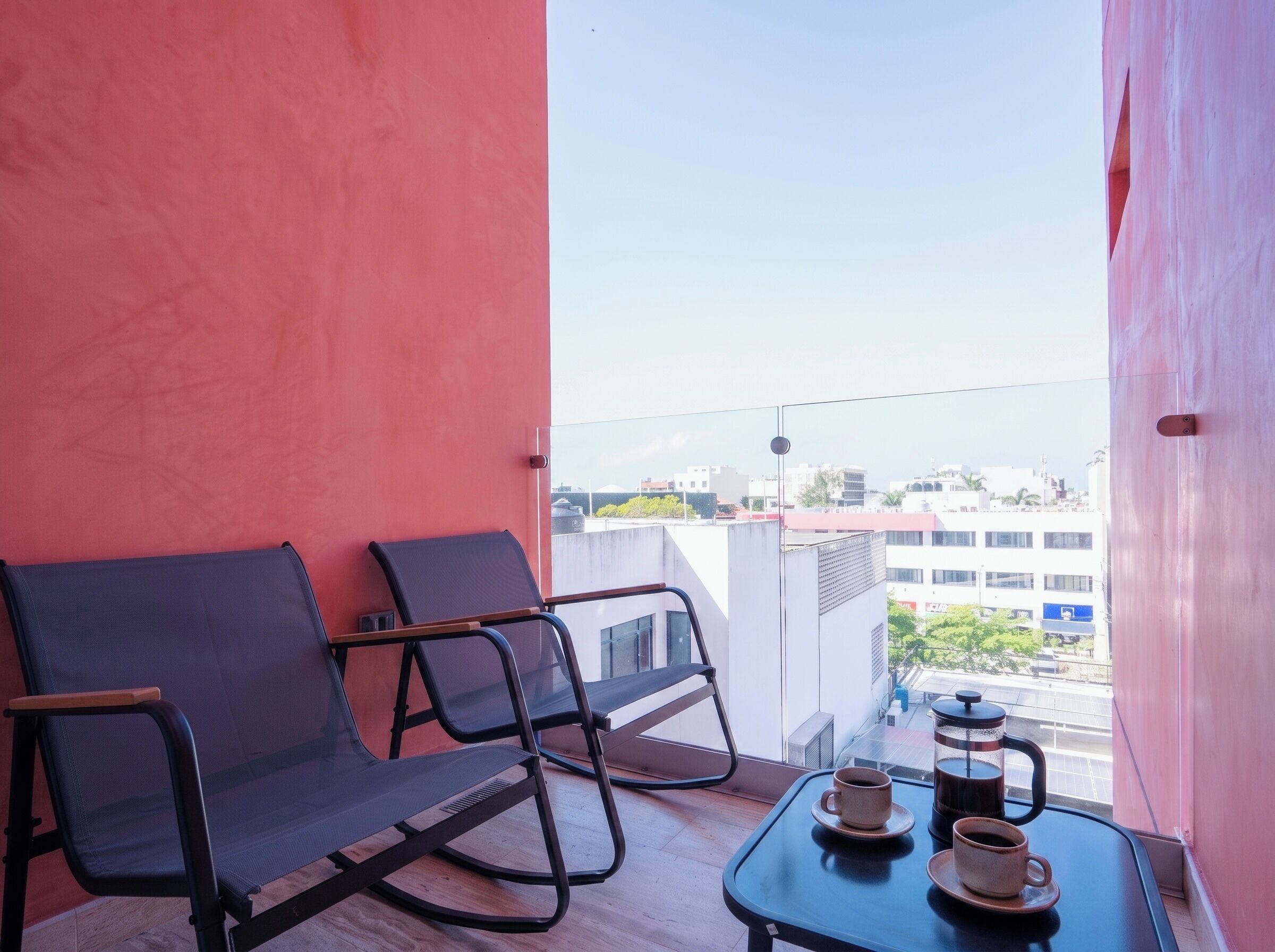 En balkon med to stole, et bord med to kopper kaffe og udsigt over byen.