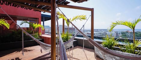 A rooftop terrace with a wooden pergola, a hammock, and potted plants.