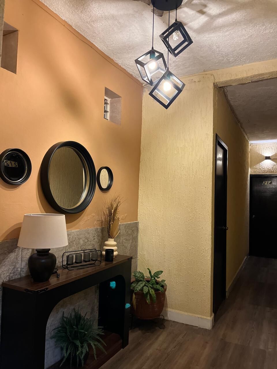 A hallway with a wooden floor, a black-framed mirror, a lamp, and a potted plant.