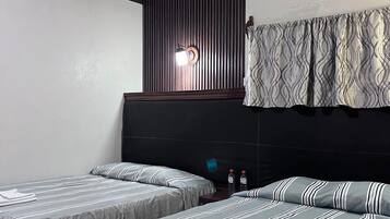 Quarto de hotel com duas camas, ar-condicionado fixado na parede e janela com cortinas estampadas.