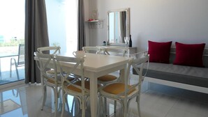 Un comedor con una mesa y sillas blancas, una lámpara de araña, un sofá con cojines rojos y un espejo grande en la pared.