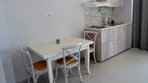 Una pequeña kitchenette con estufa, lavamanos y armarios. Hay una mesa con dos sillas y un pequeño recipiente azul encima.