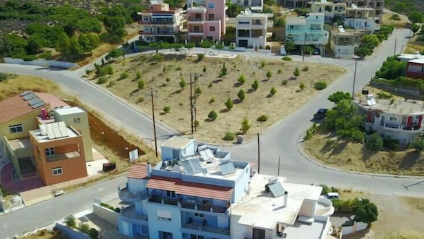 Zona residencial con un edificio blanco destacado, de techos planos y con balcón, rodeado de casas más pequeñas y una calle.
