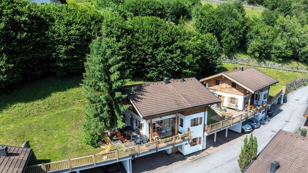 Ein zweistöckiges Chalet mit Balkon, überdachter Auffahrt und Parkplatz.