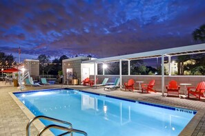 Ein Schwimmbecken mit Liegestühlen und einem überdachten Bereich, umgeben von einer Pflasterterrasse.