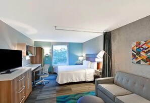 Ein Hotelzimmer mit Bett, Schreibtisch, Fernseher und einer Couch.