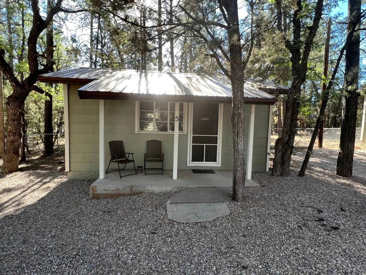 A small building with a metal roof, two chairs outside, and a gravel driveway.