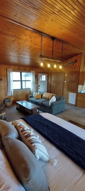 A cozy cabin interior with a sofa, a bed, and a dining table. - Riverfront Blue Heron Cabin on the Kings River (Berryville)