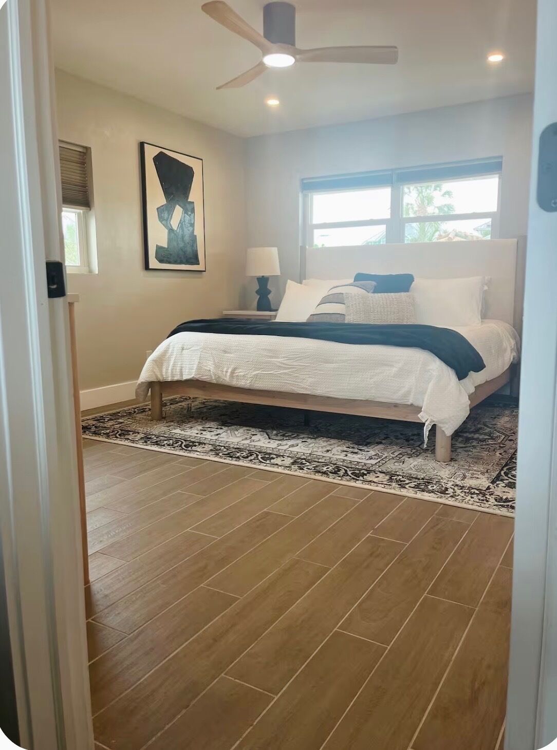 Un dormitorio con cama, ventilador de techo, ventana y alfombra.