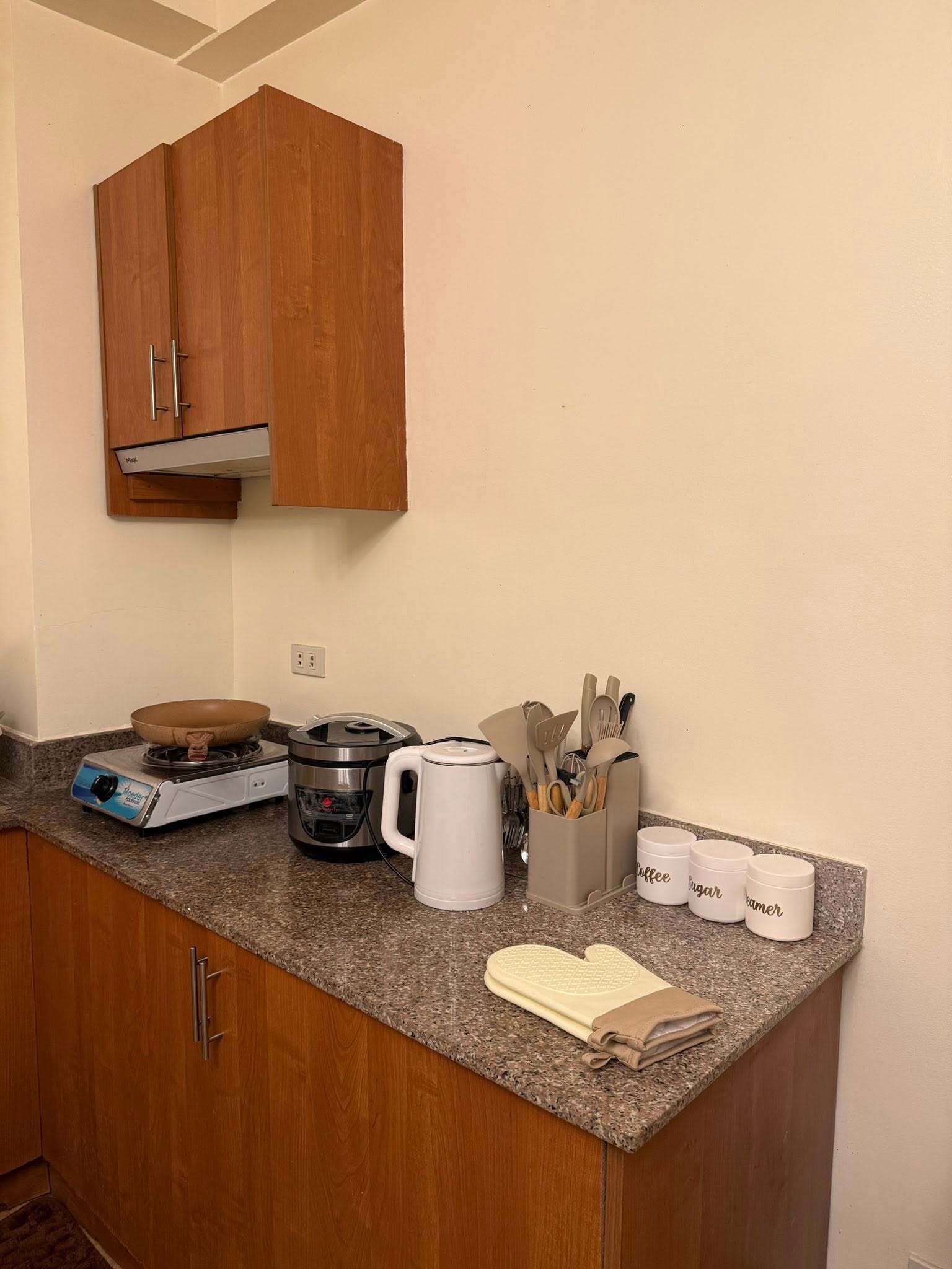 Una pequeña kitchenette equipada con estufa, cafetera y utensilios de cocina.