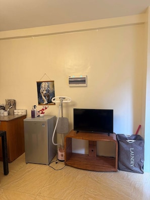 A compact living space with a kitchenette, a television, a small refrigerator, and a vacuum cleaner. - Boracay Affordable Stay (Malay)