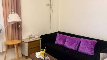 A living room with a black sofa, a wooden coffee table, a lamp, a small side table, and a wall-mounted air conditioner.