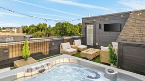 Eine Dachterrasse mit Whirlpool, Korbmöbeln und einem Flachbildfernseher.