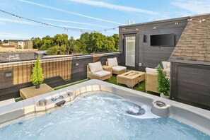 Eine Dachterrasse mit Whirlpool, Korbmöbeln und einem Flachbildfernseher.