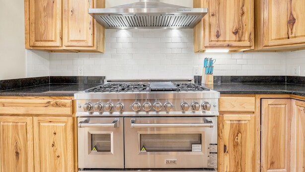 Cocina con gabinetes de madera, extractor de acero inoxidable, estufa a gas y horno empotrado.