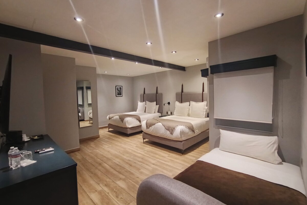 Una habitación de hotel moderna con una cama grande, una cama más pequeña, un escritorio con una silla y un espejo.
