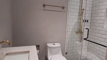 Un baño con inodoro blanco, ducha con puerta de cristal y lavamanos de mármol.