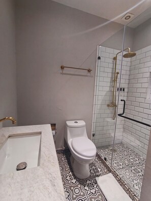 Ett badrum med en vit toalett, en dusch med glasdörr och ett handfat i marmor.