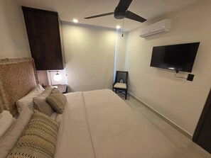 Ein Hotelzimmer mit Bett, Sessel, Fernseher, Klimaanlage und Deckenventilator.