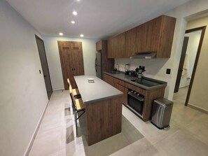A modern kitchen with wooden cabinets, a central island, and a built-in oven. - Condo 2 recámaras a pasos de playa Santa Cruz (Bahía de Santa Cruz Huatulco)