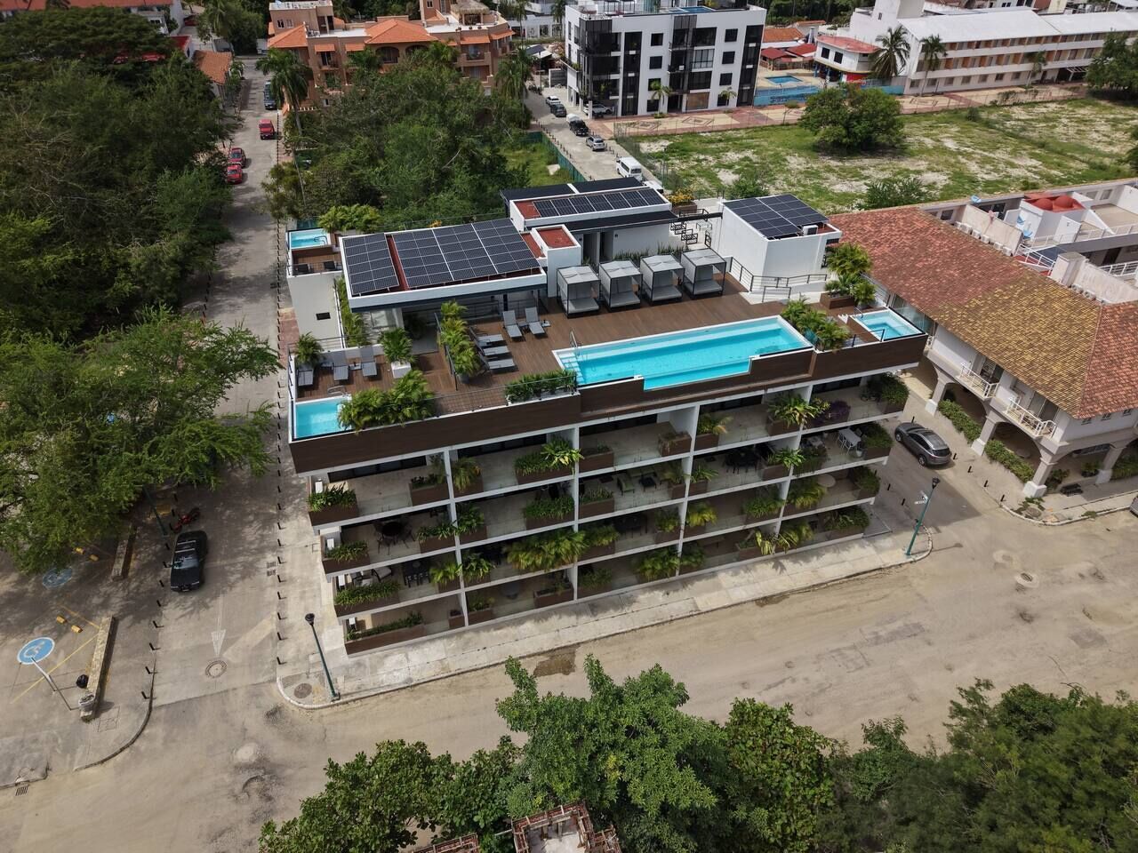 Ein mehrstöckiges Gebäude mit Pool auf dem Dach, Solaranlage und Parkplatz.