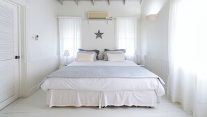 A bedroom with a large bed, white walls, a ceiling fan, and a star decoration. - Stylish luxury traditional-style poolside villa nr. beach. Two ensuite bedrooms. (Porters)