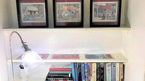 A bookshelf with books, a desk lamp, and three framed pictures on the wall. - Stylish luxury traditional-style poolside villa nr. beach. Two ensuite bedrooms. (Porters)