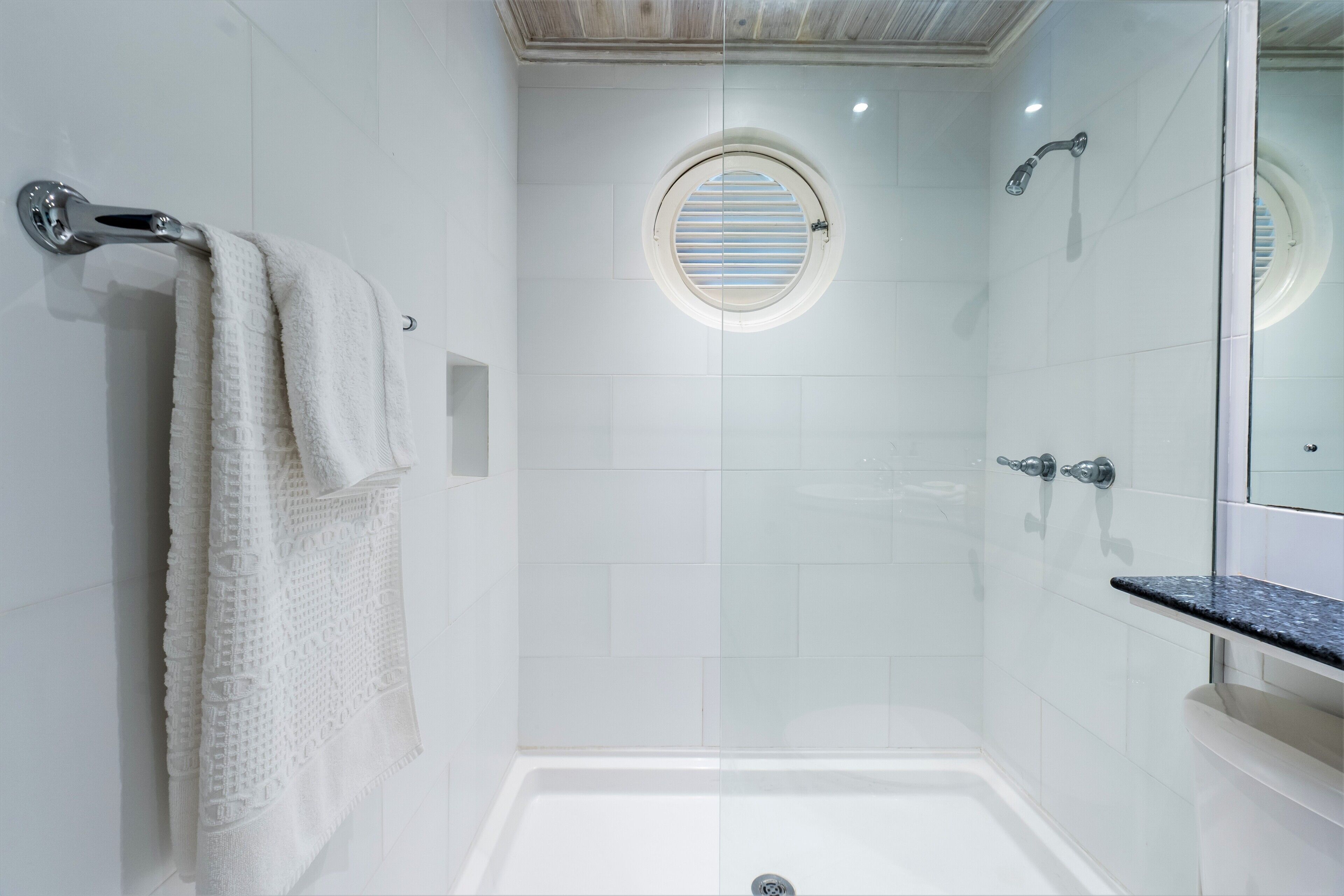 A modern bathroom with a glass-enclosed shower, a round window, and a white bathtub.