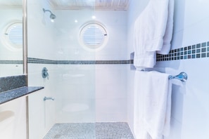 Ein modernes Badezimmer mit einer Duschkabine aus Glas, einem runden Dachfenster und Fliesenboden.