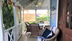 A covered porch with wicker furniture and a wooden door. - Stylish luxury traditional-style poolside villa nr. beach. Two ensuite bedrooms. (Porters)