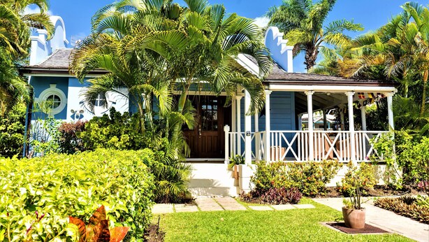 A house with a porch, surrounded by lush greenery and palm trees. - Stylish luxury traditional-style poolside villa nr. beach. Two ensuite bedrooms. (Porters)