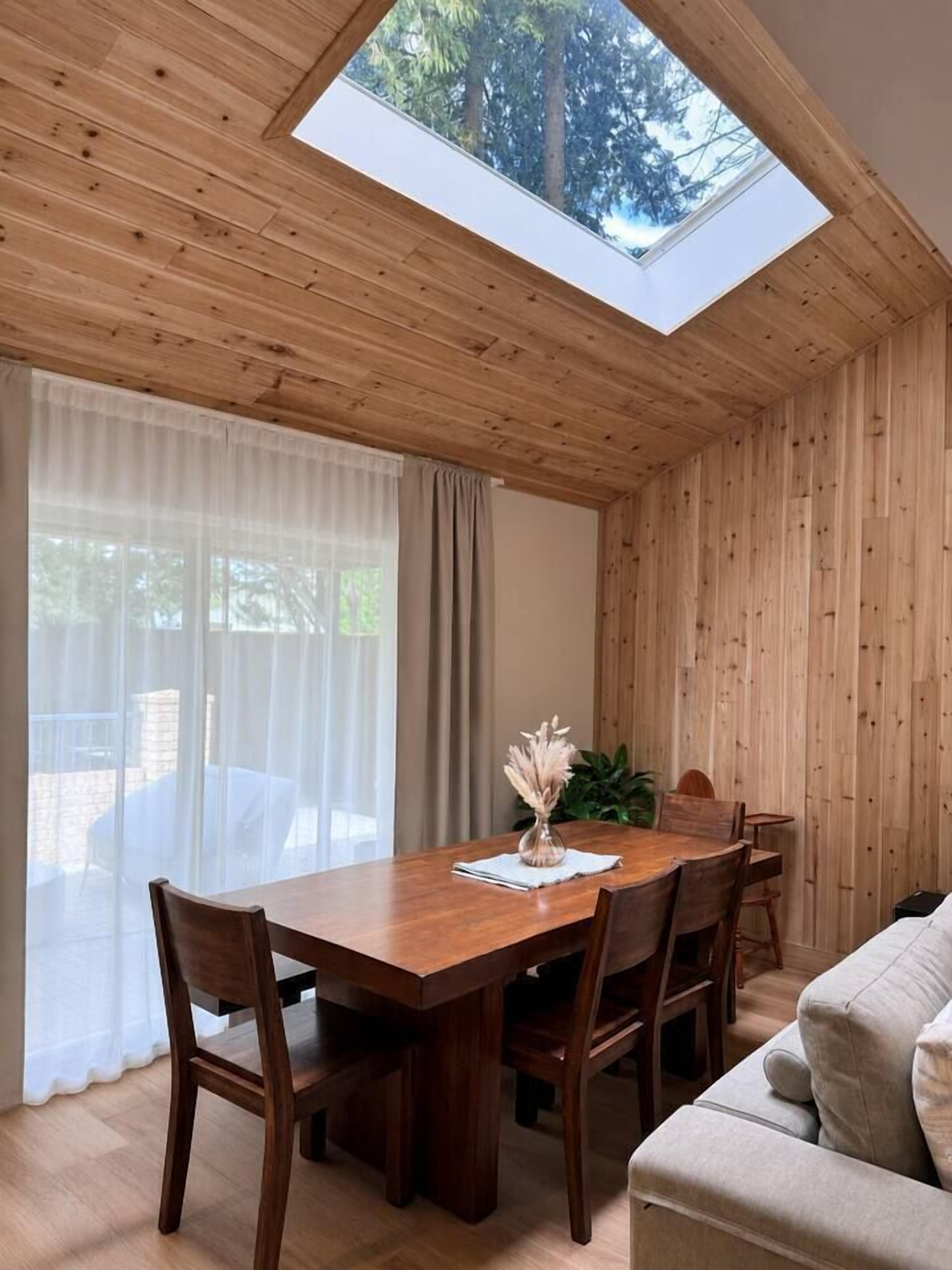 Uma área de refeições com mesa e cadeiras de madeira, um claraboia e vista para o exterior.