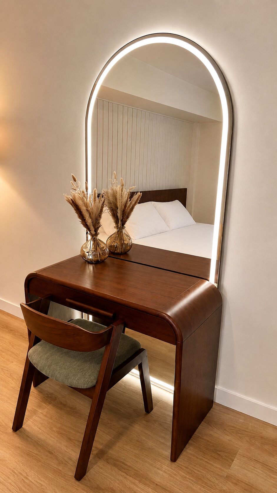 A wooden vanity with a mirror, a chair, and a bedside table with a lamp.
