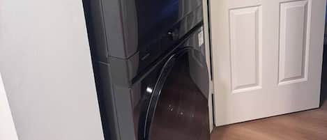 Una habitación pequeña con lavadora y secadora integradas, una puerta blanca y piso de madera.