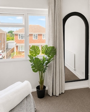 A room with a window, a potted plant, a bed, and a door.