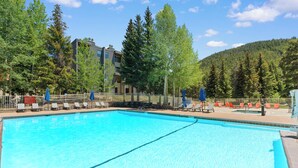 A swimming pool with lounge chairs and a fence, surrounded by trees and a building. - Modern 3br Condo in Keystone (Keystone)