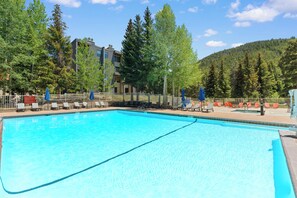 A swimming pool with lounge chairs and a fence, surrounded by trees and a building. - Modern 3br Condo in Keystone (Keystone)