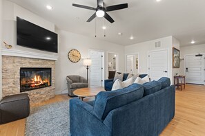 A living room with a fireplace, a flat-screen TV, a ceiling fan, and a blue sofa. - Modern 3br Condo in Keystone (Keystone)